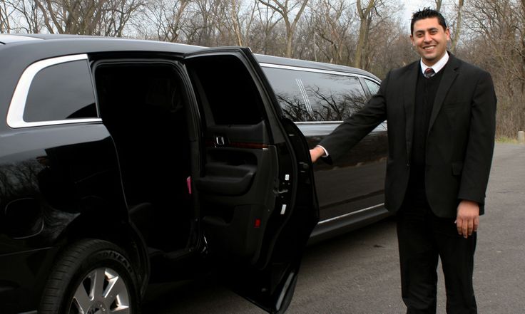 Professional chauffeur holding open the rear door of a black SUV